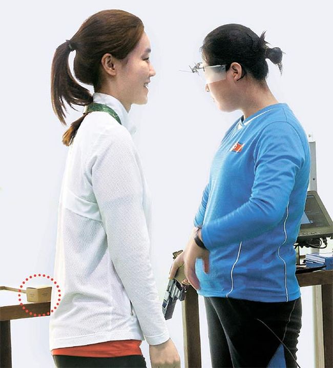 South Korean shooter Hwang Seongeun is giving North Korean shooter Jo Yong-suk a box of snack.