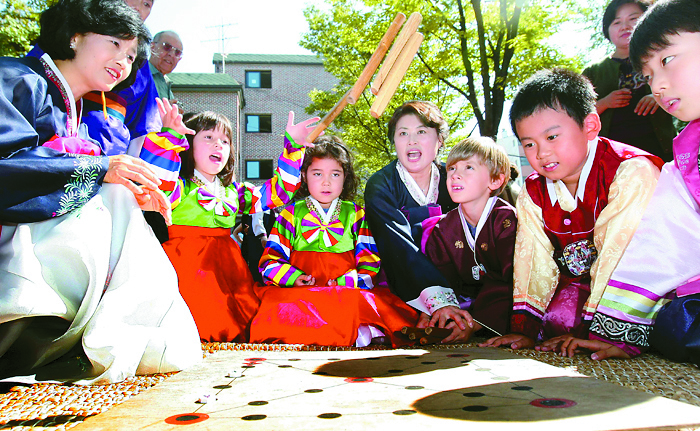 A group of children dressed in traditional Hanbok play the traditional four-stick board game, yutnori, on Seollal. Provided by Korea.net