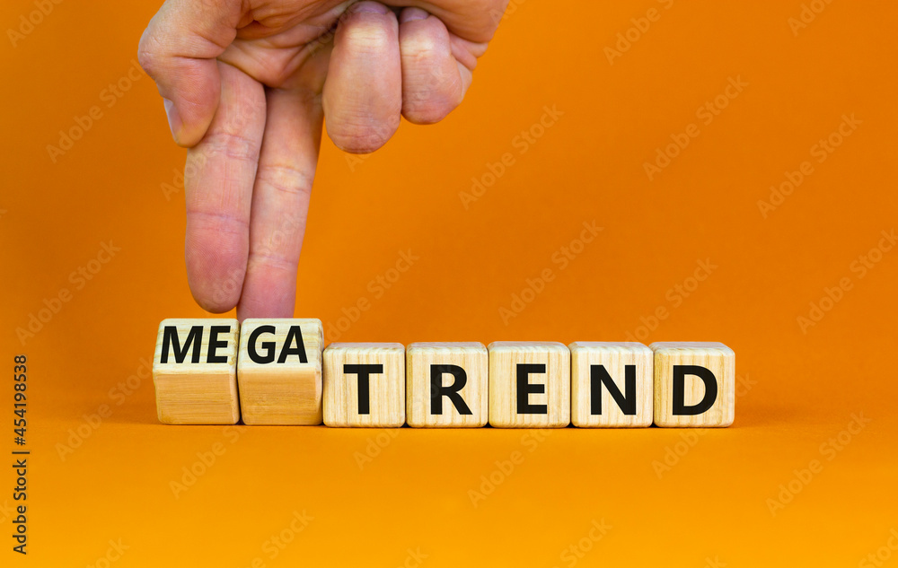 Trend or megatrend symbol. Businessman turns wooden cubes and changes words trend to megatrend. Beautiful orange table, orange background, copy space. Business, trend or megatrend concept.