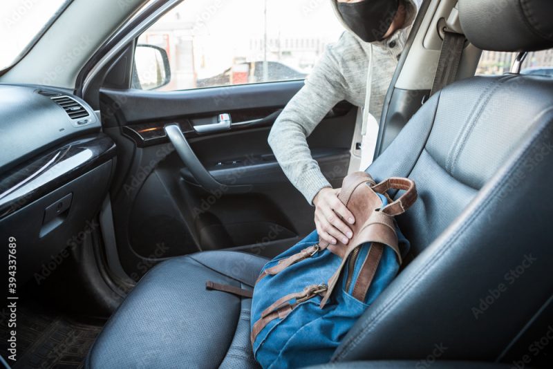 Male thief stealing bag through the opened door of car, man dressed black facemask