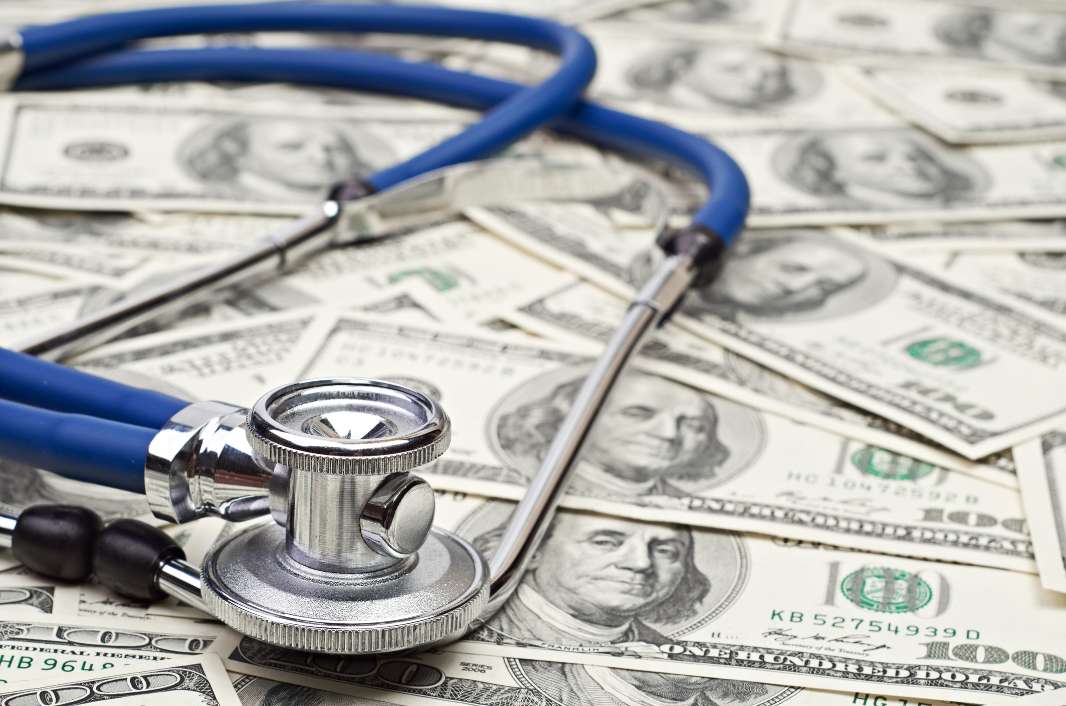 Stethoscope resting on stack of hundred dollar bills symbolizing Medicaid budget cuts