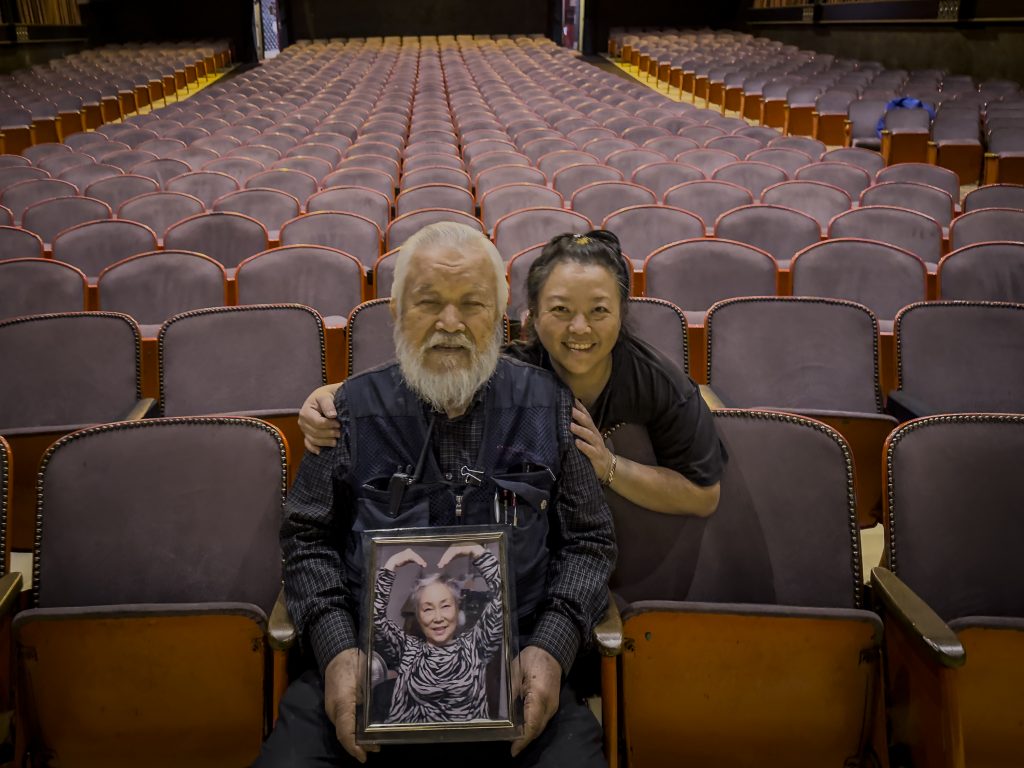 Judy Kim and John Kim seated inside Gardena Cinema holding Nancy Kim photo